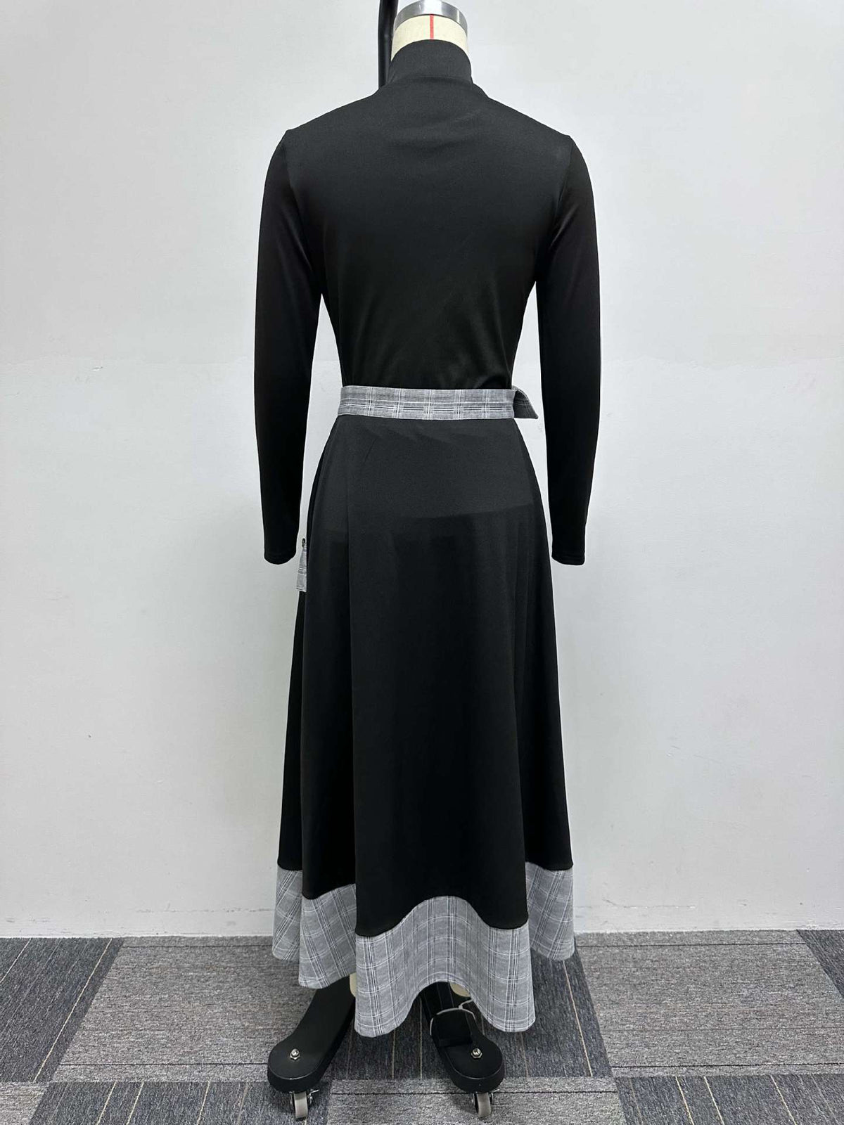 Back view on a mannequin of a black long-sleeved top and black skirt with grey plaid waist and hem panels.