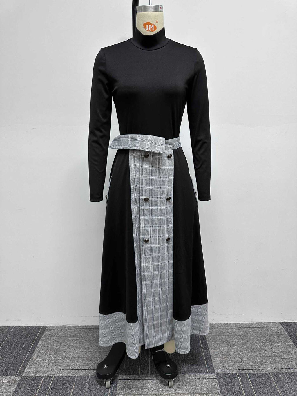 Mannequin wearing a black long-sleeved high-neck top and a black and grey plaid skirt with button detailing and a front opening.